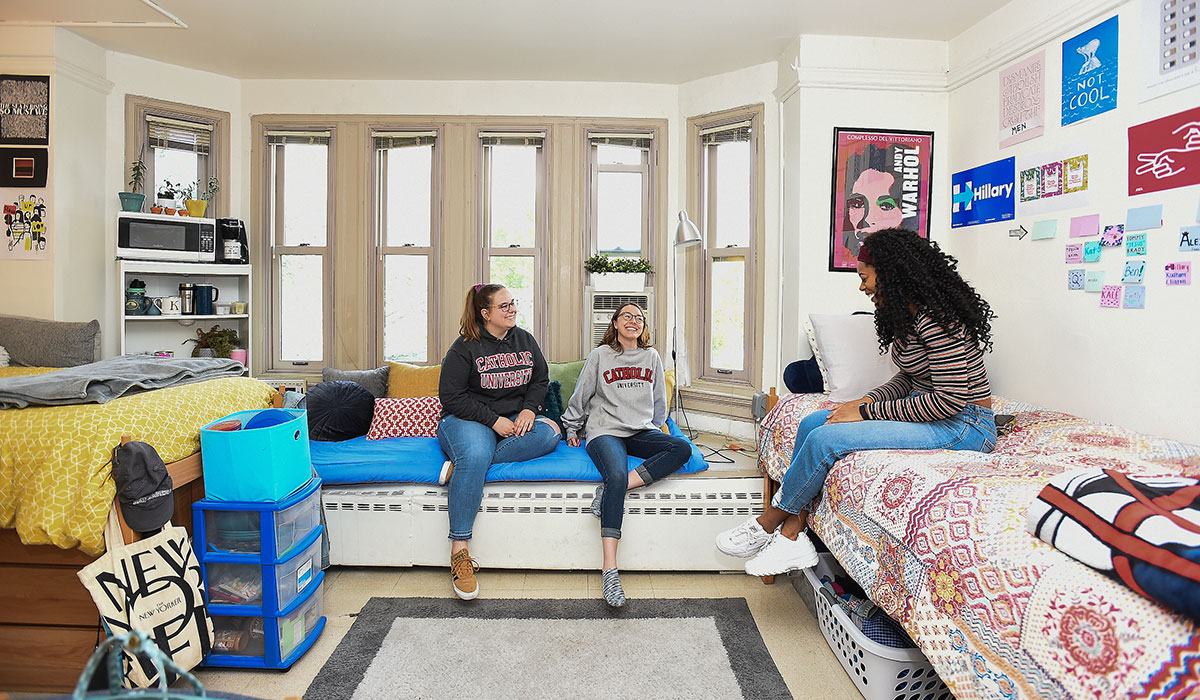 Three female students sitting on beds in their room, talking